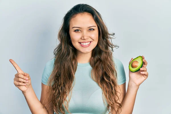 Ung Latinamerikansk Flicka Håller Mitten Avokado Ler Glad Pekar Med — Stockfoto