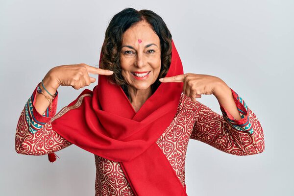 Middle age hispanic woman wearing tradition sherwani saree clothes smiling cheerful showing and pointing with fingers teeth and mouth. dental health concept. 