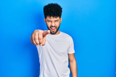 Sakallı, beyaz tişörtlü genç bir Arap, kameraya kızgın ve sinirli bir şekilde bakıyor. 