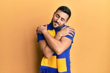 Genç İspanyol futbolcu holigan amigoluk oyunu. Kendine sarılıyor, mutlu ve pozitif, kendinden emin gülümsüyor. Sevgi ve özgüven. 