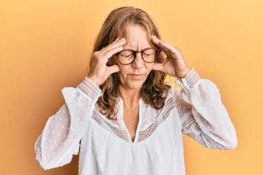 Sarı arka plan üzerine gündelik kıyafetler giyen orta yaşlı sarışın kadın, baş ağrısı, stres yüzünden. migren ağrısı. 