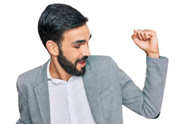 Genç İspanyol adam iş kıyafetleri giymiş mutlu ve neşeli dans ediyor, gülümsüyor rahat ve kendinden emin bir şekilde müzik dinliyor. 