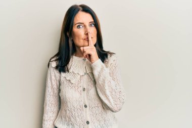 Orta yaşlı esmer kadın gündelik kıyafetler giyip parmakları dudaklarında sessiz olmak istiyor. sessizlik ve gizli konsept. 