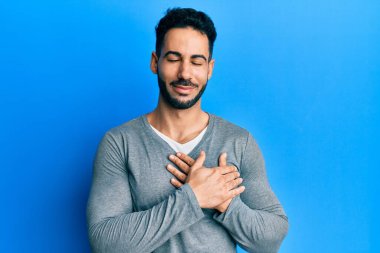 Gündelik beyaz tişört giyen, elleri göğsünde gülümseyen, gözleri kapalı, yüzünde minnet ifadesi olan genç İspanyol bir adam. sağlık kavramı. 