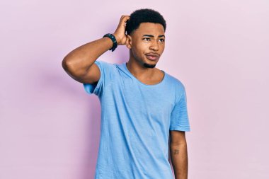 Gündelik mavi tişört giyen genç Afro-Amerikan bir adam kafasını karıştırıyor ve soru soruyor. Şüpheyle kararsız, kafa kafaya düşünerek. Düşünceli kavram. 