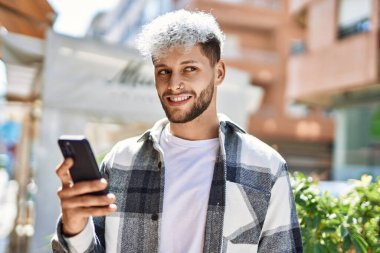 Genç İspanyol adam şehirde akıllı telefon kullanarak mutlu gülümsüyor..