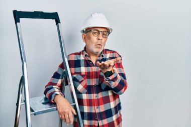 İnşaat merdivenlerine yakın, kasketli yakışıklı yakışıklı bir adam kameraya bakıp havada öpüşüyor ve güzel ve seksi oluyor. aşk ifadesi. 