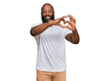 Gündelik beyaz tişört giyen, aşık gülümseyen, elleriyle kalp sembolü yapan genç Afro-Amerikan bir adam. romantik kavram. 