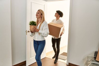 Mutlu bir şekilde gülümseyen genç bir çift yeni evine karton kutuyla giriyor..
