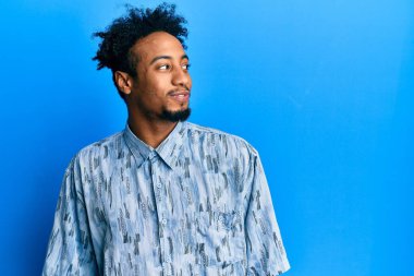 Sakallı, sıradan giyinmiş, gülümseyen ve kafasını çeviren genç Afrikalı Amerikalı bir adam.. 