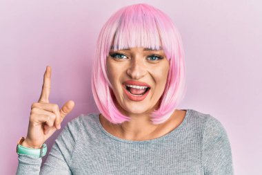 Pembe peruklu genç beyaz kadın başarılı bir fikri işaret ediyor. Heyecanlı ve mutlu. Bir numara.. 
