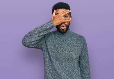 Genç, Afro-Amerikan bir adam günlük giysiler giymiş. Şoka girmiş, yüzünü ve gözlerini kapamış, utanmış bir ifadeyle parmaklarının arasından bakıyor.. 