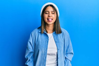 Tatlı yün şapkalı genç Latin kadın komik bir ifadeyle mutlu bir şekilde dilini dışarı çıkarıyor. duygu kavramı. 