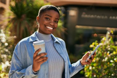 Genç Afrikalı Amerikalı kadın akıllı telefon kullanıyor ve şehirde kahve içiyor.