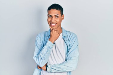 Elleri çenesinde gündelik giysiler giyen genç Afro-Amerikan adam soru sormayı düşünüyor, düşünceli bir ifade. Düşünceli bir yüzle gülümsüyor. şüphe kavramı. 