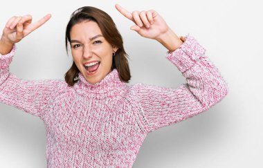 Yün kazak giyen genç beyaz kız şaşırmış, şaşırmış ve parmaklarıyla işaret ediyor ve kollarını kaldırıyordu.. 