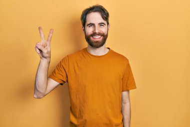 Sakallı, sıradan sarı tişörtlü, beyaz bir adam iki numaralı parmaklarıyla onu gösterirken, kendinden emin ve mutlu gülümsüyor.. 