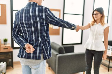 İki iş adamı mutlu bir şekilde el sıkışırken gülümsüyor. Ofiste şans dileyerek duran bir adam..