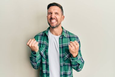 Sakallı yakışıklı, sıradan kıyafetler giyen, mutlu ve heyecanlı kolları havada, gülümseyen ve başarı çığlıkları atan, kazanan bir jest yapan bir adam. kutlama konsepti. 