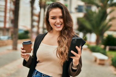 Genç İspanyol kadın akıllı telefon kullanıyor ve şehirde kahve içiyor..