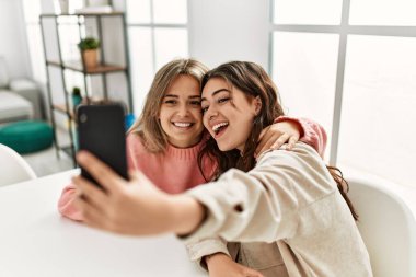 Genç çift mutlu bir şekilde gülümsüyor. Evdeki akıllı telefonun yanında selfie çekiyorlar..