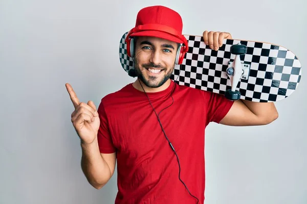 Jovem Hispânico Usando Fones Ouvido Segurando Skate Sorrindo Feliz Apontando — Fotografia de Stock