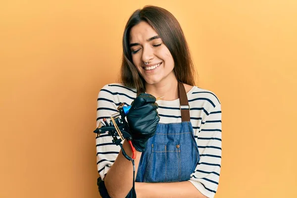 Young hispanic woman tattoo artist wearing professional uniform and gloves smiling and laughing hard out loud because funny crazy joke.