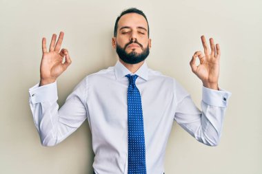 Sakallı genç adam iş kravatı takıyor rahatla ve gözleri kapalı gülümse parmaklarıyla meditasyon hareketi yapıyor. yoga konsepti. 