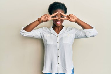 Genç Afro-Amerikan kızı gündelik kıyafetler giyip barış sembolü yapıyor. Yüzünde parmaklarıyla gülümsüyor ve zaferini gösteriyor. 