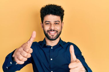 Sakallı, günlük gömlekli genç bir Arap, el hareketleriyle olumlu bir jest yapmayı onaylıyor, gülümsüyor ve başarı için seviniyor. kazanan jest. 