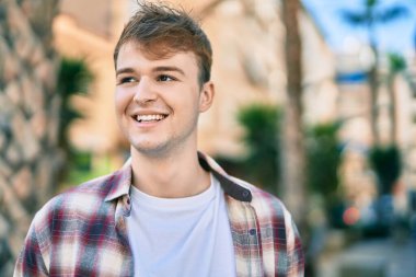 Genç beyaz adam gülümseyerek şehirde mutlu mesut duruyor..