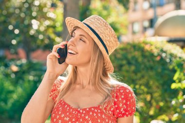 Yaz tarzı giyinen genç sarışın kadın parkta akıllı telefondan konuşuyor.