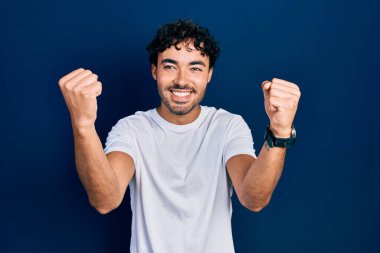 Gündelik beyaz tişört giyen genç İspanyol adam gururla bağırıyor, zaferi kutluyor ve kollarını kaldırarak çok heyecanlanıyor. 