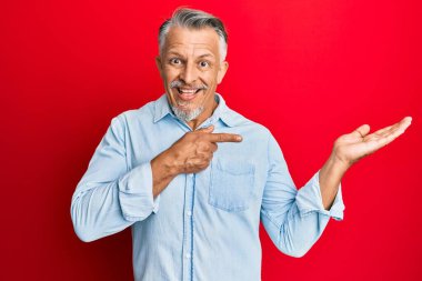 Orta yaşlı, gri saçlı, sıradan kıyafetler giyen bir adam kameraya hayret ediyor ve gülümsüyor.. 