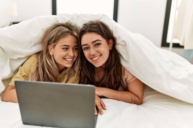 Yatakta çarşafla film izleyen genç çift..