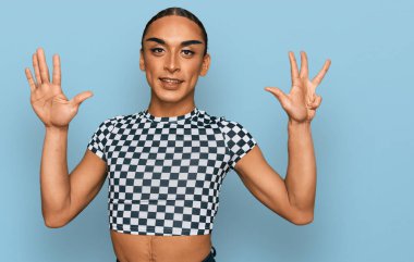 Makyaj yapan, uzun saçlı, modern kıyafetler giyen İspanyol transseksüel adam dokuz numaralı parmaklarını gösterip gülümserken mutlu ve kendinden emin.. 