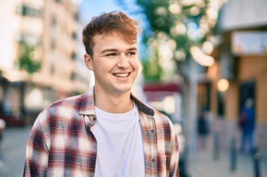 Genç beyaz adam gülümseyerek şehirde mutlu mesut duruyor..