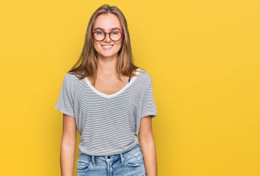 Güzel, genç, sarışın bir kadın. Günlük kıyafetler ve gözlük takıyor. Yüzünde mutlu ve havalı bir gülümseme var. şanslı kişi. 