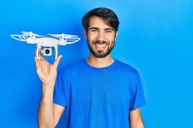 İHA 'yı tutan genç İspanyol adam pozitif ve mutlu görünüyor. Duruyor ve gülümsüyor. Kendine güvenen bir gülümsemeyle dişlerini gösteriyor. 