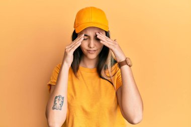 Genç İspanyol kadın teslimat üniforması giyiyor ve stres yüzünden başı ağrıyan bir şapka takıyor. migren ağrısı. 