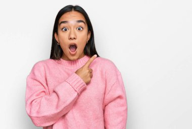 Kış süveteri giyen genç Asyalı kadın parmaklarını yana doğru göstererek şaşırdı, ağzı açık hayret içinde kaldı.. 