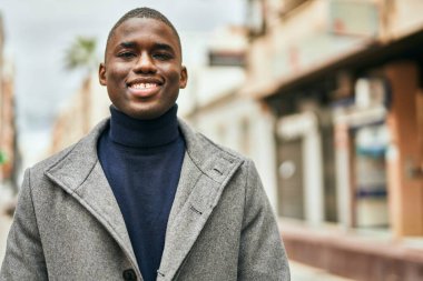 Genç Afrikalı Amerikalı adam gülümseyerek şehirde mutlu mesut duruyor.