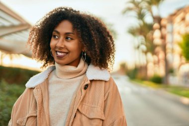 Genç Afrikalı Amerikalı kadın gülümseyerek şehirde mutlu mesut duruyor..