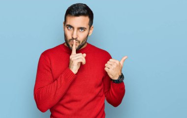 Gündelik giysiler giyen genç İspanyol adam sessiz olmak istiyor. Parmakları dudaklarında, elleri yandan işaret ediyor. sessizlik ve gizli konsept. 