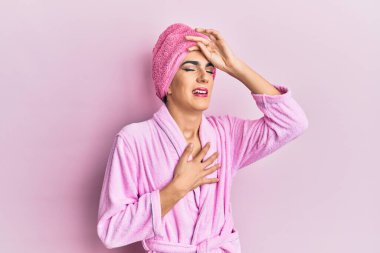 Kadın elbisesi giyen genç adam makyaj havlusu ve bornozla hasta, grip ve soğuk algınlığı için alnına dokunuyor. 