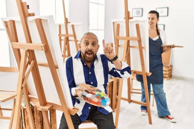 Sanat stüdyosundaki kıdemli sanatçı şaşırmış, şaşırmış ve parmaklarıyla işaret ederek kollarını kaldırmıştı.. 