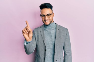 İş kıyafetleri giymiş genç bir Arap bir fikir veya soruyla gülümsüyor ve mutlu bir yüzle işaret ediyor. 