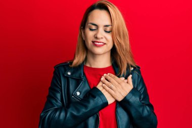 Siyah deri ceket giyen, elleri göğsünde gülümseyen, gözleri kapalı, yüzünde minnet ifadesi olan İspanyol bir kadın. sağlık kavramı. 