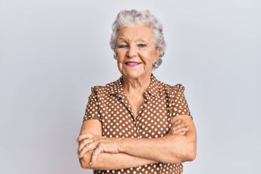 Yaşlı, gri saçlı, sıradan kıyafetler giyen mutlu yüzlü, kollarını kavuşturup kameraya bakan bir kadın. pozitif kişi. 