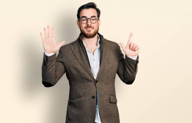 İş ceketi ve gözlük takan genç İspanyol adam yedi numaralı parmaklarını gösterip işaret ederken kendinden emin ve mutlu gülümsüyor.. 
